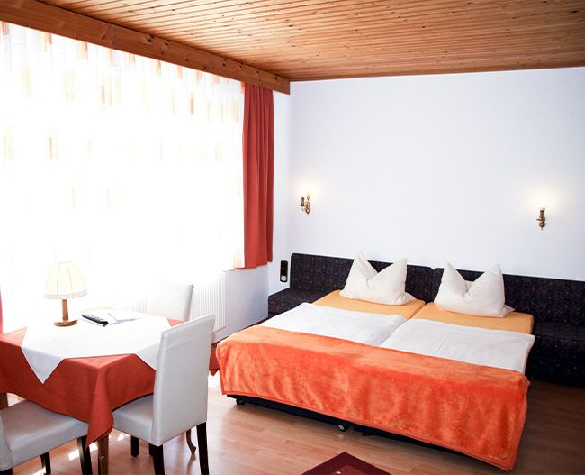 Zimmer mit orangener Bettwäsche, Tisch und Stühlen